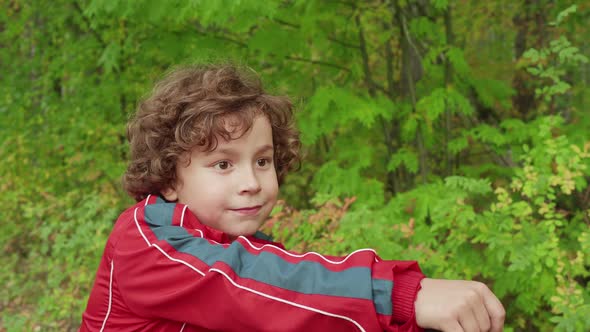 Portrait Curly Boy with Brown Hair on Bicycle in Green Park