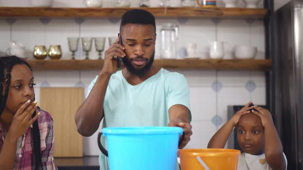 Worried African Family Collecting Water Leaking From Ceiling While Father Calling Plumber at Home