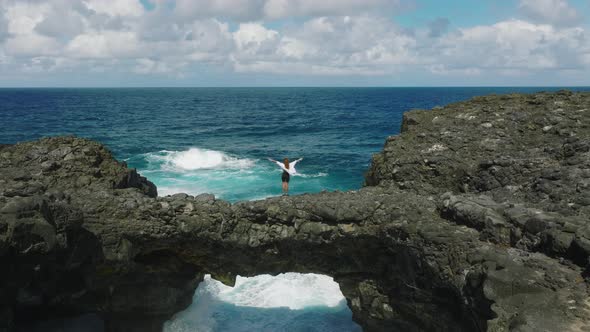 A Young Girl in a White Dress Stands on the Rocks on the Shore of the Indian Ocean