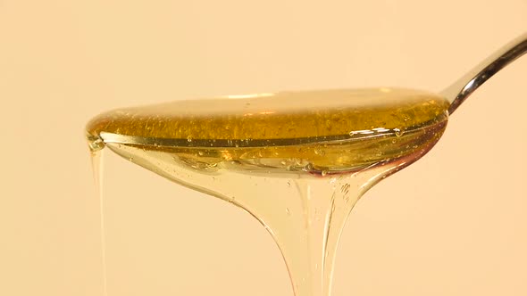 Pouring fluid honey from metal spoon over beige background