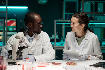 Two Biracial Researchers Sitting in Lab Discussing Synthetic Meat