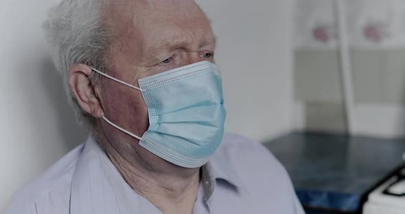 An Elderly Man with a Coronavirus Coughs Up in a Mask and Looks at the Camera