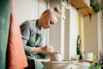 Woman potter moulding walls of clay ware on potters wheel