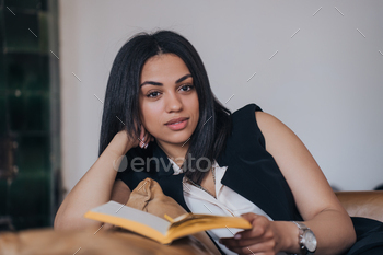 Thoughtful woman reading a book, resting on a leather sofa in a stylish room.