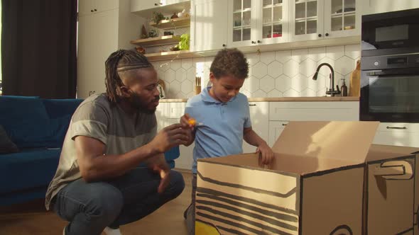 Cute African American Son and Father Playing with Toy Cardboard Car at Home