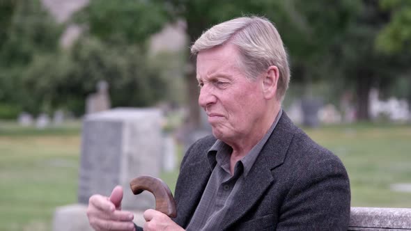 Elderly man sitting in cemetery lost in thought