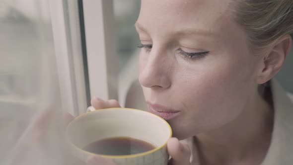 Blond woman with cup of tea at window