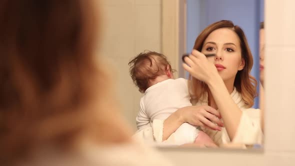 Mother with a child in hands in bathroom make a face massage