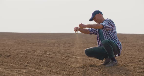 Farmer Examining Soil Quality While Crouching at Farm