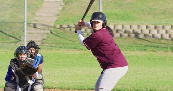 Diverse group of female baseball players playing on the field, hitter swinging for pitched ball