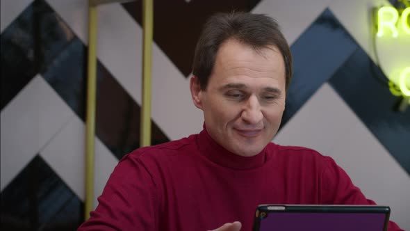 Smiling Handsome Middleaged Man Chutting in Cafe with Tablet