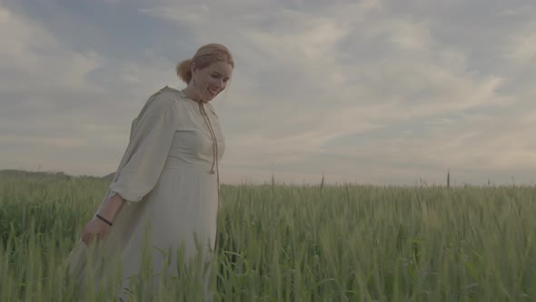 A Young Beautiful Girl in Ethnic Dress Walks Along the Green Field of Wheat