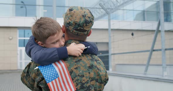 Back View of Son Putting Hands Around Military Father Neck.