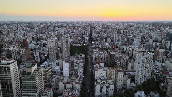 Dolly in flying over long avenue at sunset in the middle of busy Belgrano neighborhood, Buenos Aires