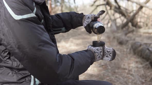 Traveling alone with a map. A tourist on a walk in a forest park drinks tea from a thermos.