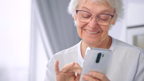 Smiling aged in glasses and blue blouse communicates with children on white smartphone