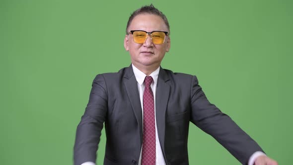 Mature Japanese Businessman Wearing Sunglasses Against Green Background