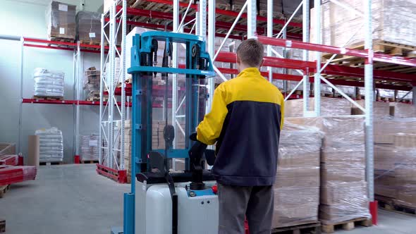 Warehouse Worker Driver in Uniform Loading Cardboard Boxes By Forklift Stacker Loader