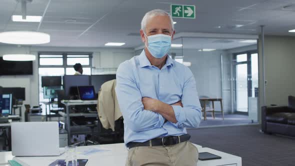 Portrait of man wearing face mask standing with his arms crossed in office