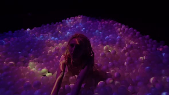 Young Woman Playing with Balls in a Dry Pool Spotlight with Abstract Video Art