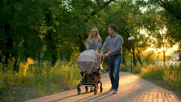 A Happy Heterosexual Couple Walks in the Park with a Baby Stroller