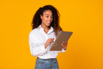 Happy young black woman using tablet computer over yellow background