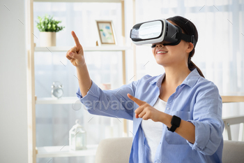 Emotional young asian woman in VR glasses sitting on couch