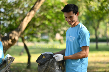Handsome male volunteer collecting garbage in public park. Charity and ecology concept