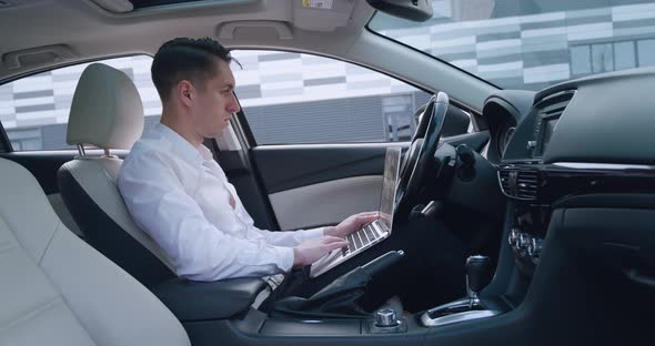 Portrait of Man Businessman Working at Laptop Computer While Sitting in the Car on the Driver's Seat
