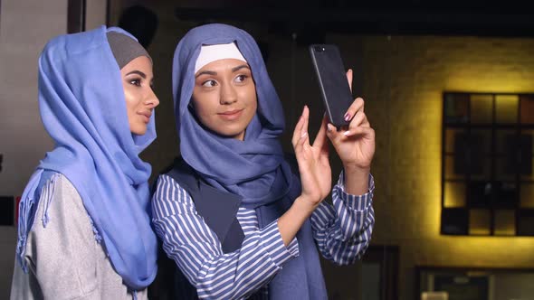 Modern Muslim Women Take Pictures on a Mobile Phone. Girls in Hijabs Talking and Smiling