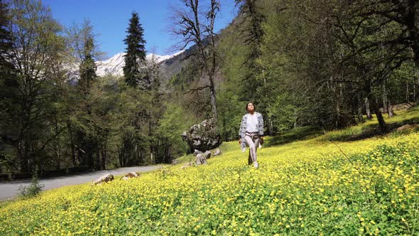 Young Woman Walks on a Green Field with Blooming Flowers on a Summer Day