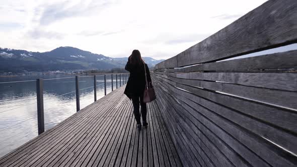 Following shot of a young asian woman walking on a wooden pier in Rapperswil, Switzerland in slow mo