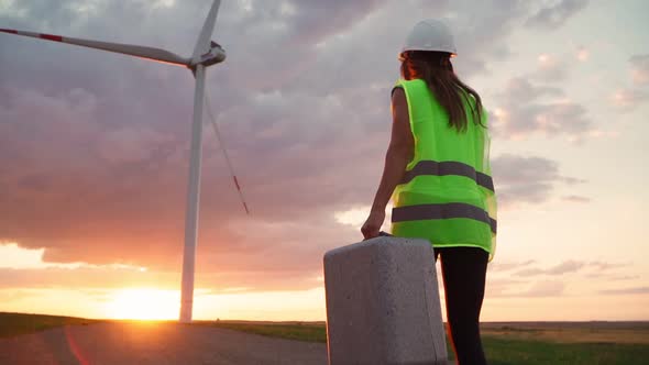 Woman Professional Engineer in uniform and helmet with special equipment in hand goes to a windmill