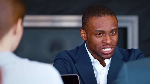 Smiling afro american businessman in suit talking with colleagues at table