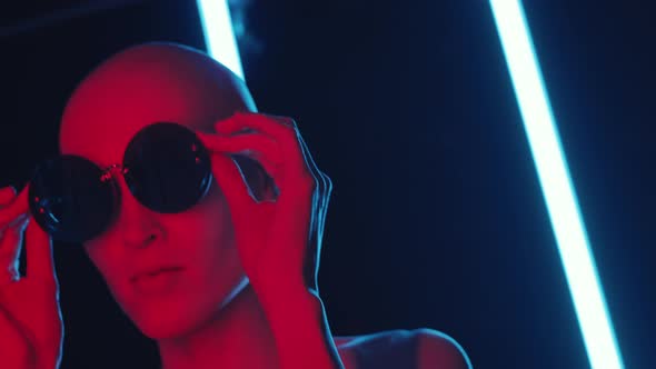 Bald Fashion Model in Round Sunglasses Posing in Blinking Neon Light