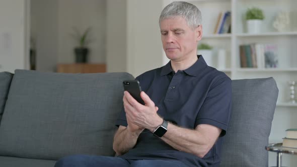 Attractive Middle Aged Businessman Using Smartphone on Sofa 