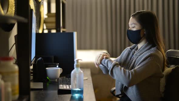 Young Asian Woman with Mask Using Hand Sanitizer While Working From Home at Night