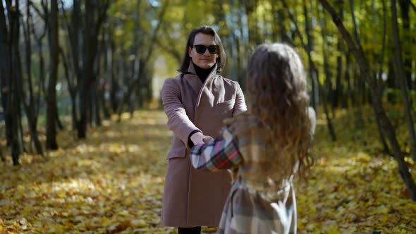 a Man and a Woman in a Coat and Dark Glasses Hold Hands and Spin Against the Background of an Autumn