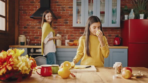 Smiling Little Girl Taking Lemon From Kitchen Table and Sniffing It