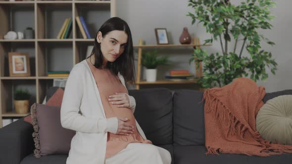 Portrait of Pregnant Woman Sitting on Sofa and Gently Touching Belly