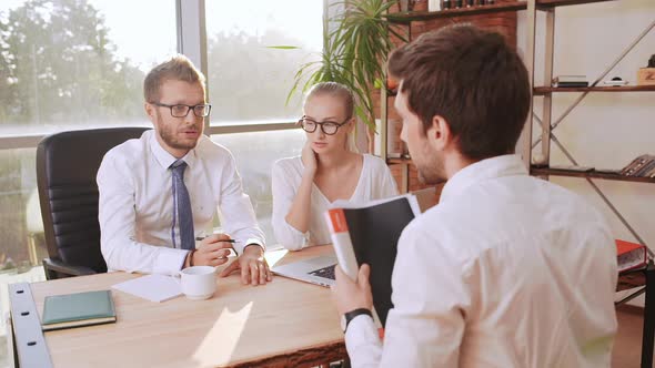 Caucasian Male Boss with Glasses and Light Bristle Sitting at Table with Female Secretary Discussing