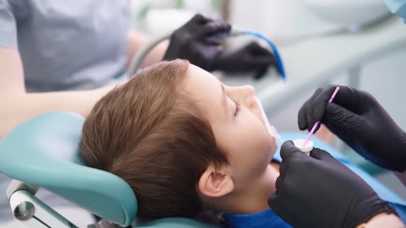 Two Woman Doctors in Medical Cap in Dental Clinic Serve the Patient Little Boy