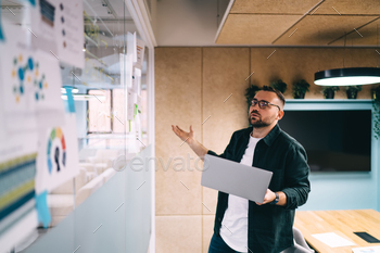 Young man standing with laptop and searching for documents in office