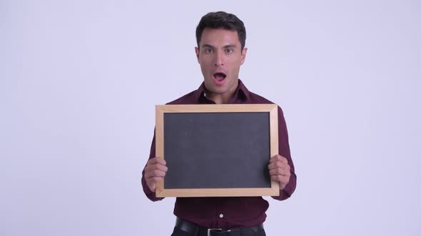 Young Happy Hispanic Businessman Holding Blackboard and Looking Surprised