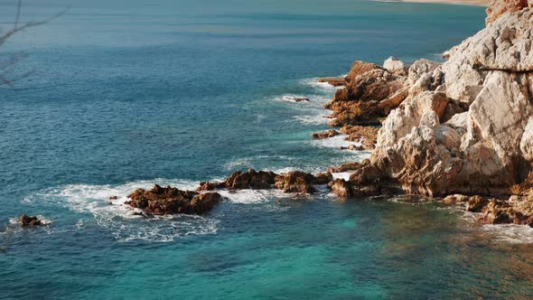 Clear turquoise sea water breaking on rocky cliff. 