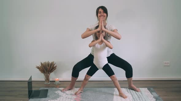 Caucasian Woman with a Girl Does Yoga Online Mom and Daughter Stand in a Chair Pose Yoga for