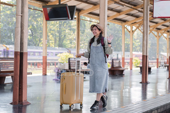Cute Asian traveler woman carrying a suitcase waiting for the train at the train station