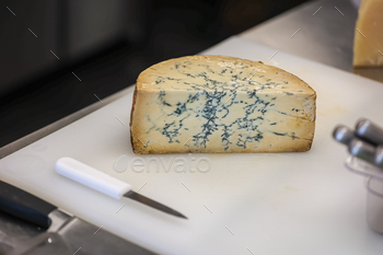 A wedge of Stilton Blue Cheese sits on a cutting board in a specialty cheese shop.