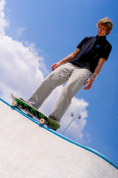 A young guy skater stands on the edge of a skate pool against a backdrop of sky and clouds