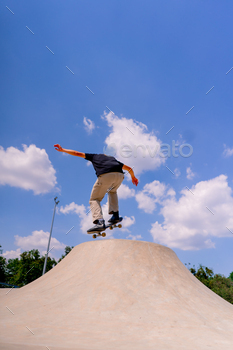 A young guy skater does a stunt on the edge of a skatepool against a backdrop of sky and clouds